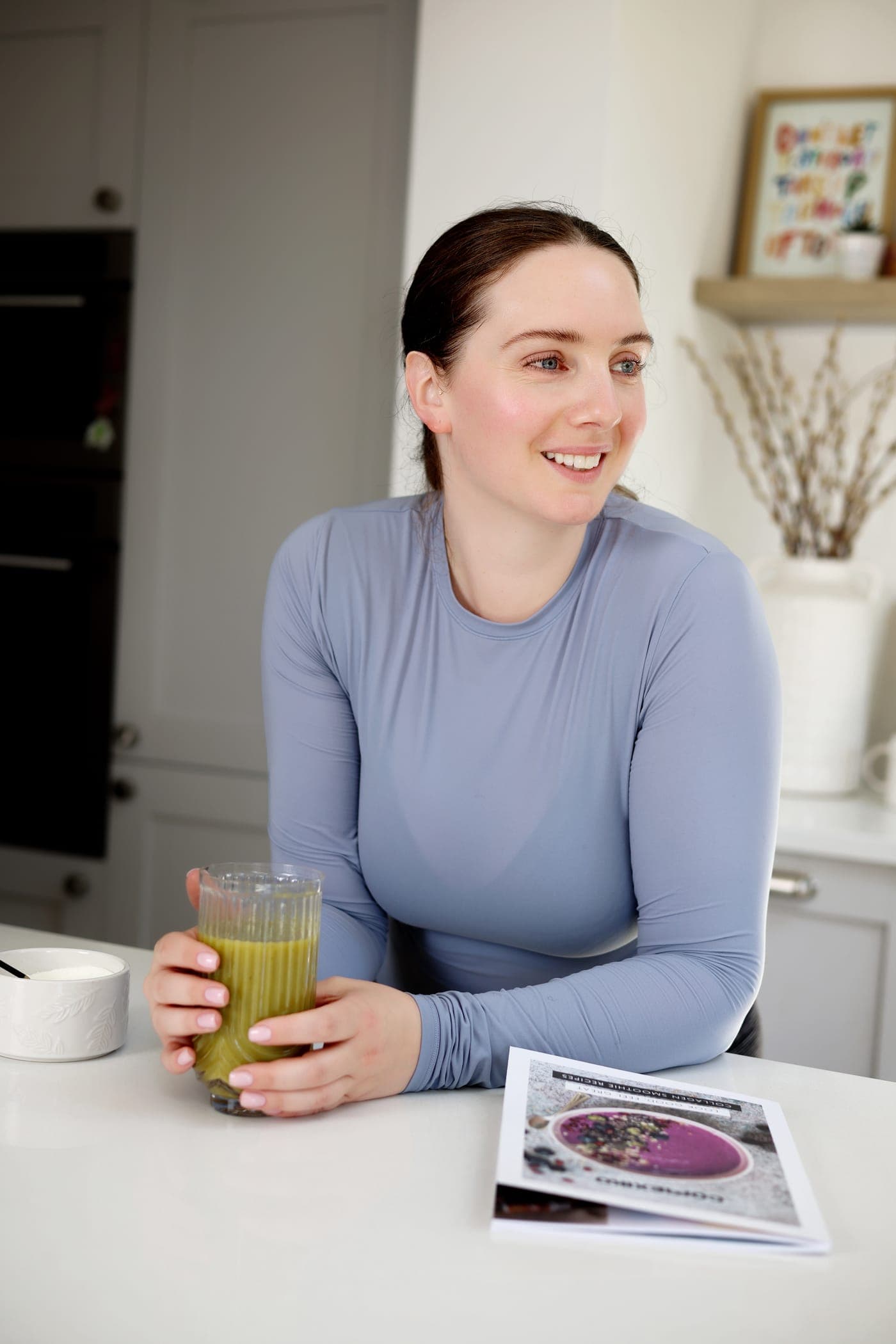 A woman with a green smoothie in her kitchen